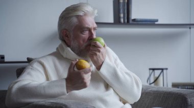 Elderly man with a gray beard sniffs lemon and Apple and does not smell clipart