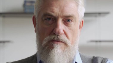 Kameraya bakan sakallı ve bıyıklı gülümseyen yaşlı bir adamın yakın plan portresi.