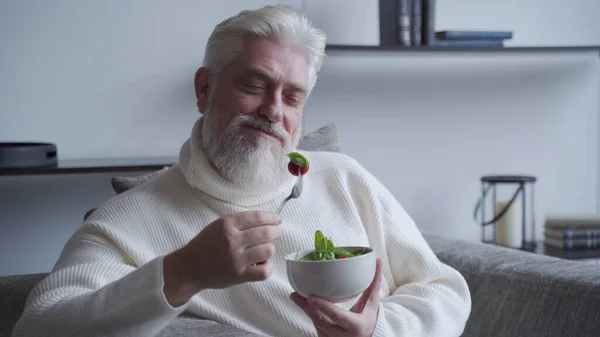 Hombre mayor se siente feliz de disfrutar de comer comida dieta ensalada fresca en el sofá —  Fotos de Stock