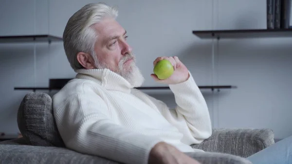 Bearded oudere man zit alleen op een stoel met een appel in zijn hand, denken — Stockfoto