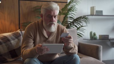 Kredi kartı ve tabletten başvuru ile online ödeme yapan emekli. Modern teknoloji ile internet ödemeleri ev satın alma kullanan yaşlı kişi