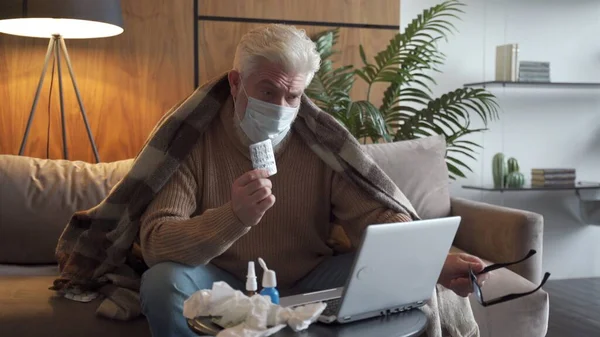 Telessaúde - um homem idoso com uma barba cinza que está doente vídeo conversando com o médico no laptop em casa — Fotografia de Stock
