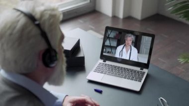 Sakallı yaşlı bir adam video bağlantısıyla doktorla bilgisayar yoluyla iletişim kurar. Karantina koşullarında tıbbi bakım. Uzaktan terapistle görüşme.