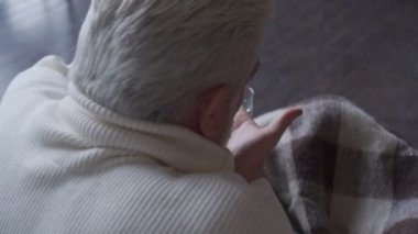 Evdeki oturma odasında ilaç içip su içen yaşlı bir adam..