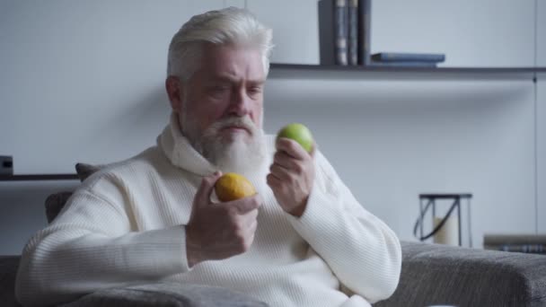 Oudere man met een grijze baard ruikt citroen en appel en ruikt niet — Stockvideo