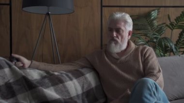 Kanepede oturan gri sakallı yaşlı bir adam lambayı açıp kapatıyor. Düşünceli yaşlı bir adam depresyondadır.
