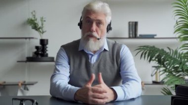 Kulaklık takmış yaşlı bir işadamı bir iş ortağıyla görüntülü görüşme yapıyor.