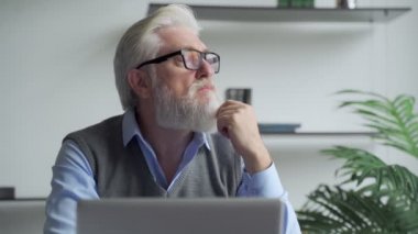 Düşünceli yaşlı iş adamı gri sakallı, sorunların çözümünü bilgisayarda bulmayı düşünüyor..