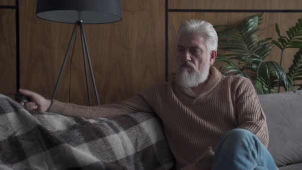 Starší muž s šedým vousem sedícím na pohovce rozsvítí a zhasne lampu. Uvažující starší muž je v depresi. — Stock video