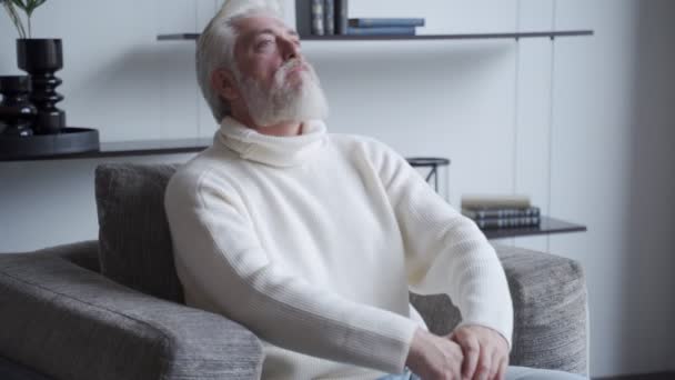 Homme mûr détendu avec une barbe grise à la maison assis dans une chaise — Video