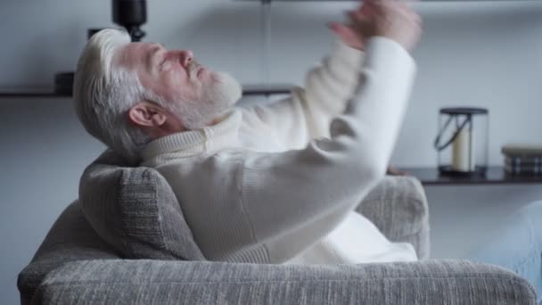 Avslappnad Mogen man med grått skägg hemma sitter i en stol — Stockvideo