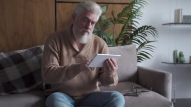 Haberleri okuyorum. Evdeki koltukta oturan gri sakallı, dijital tablet kullanan yaşlı adam.