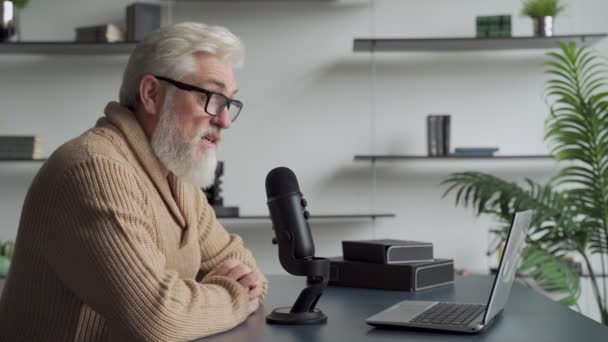 Äldre man med en grå skäggvideo bloggare talar i mikrofon. Åldrande programföretag bor i en studio — Stockvideo