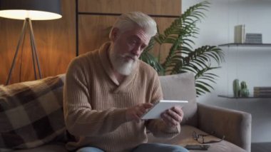 Haberleri okuyorum. Evdeki koltukta oturan gri sakallı, dijital tablet kullanan yaşlı adam.