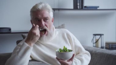 Yaşlı adam diyet yemeğinin keyfini çıkarırken kanepenin üzerinde taze salata yiyor.