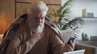 TeleHealth - gri sakallı yaşlı bir adam. Evde akıllı telefondan doktorla görüntülü sohbet ediyor.