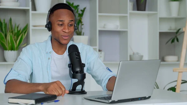 Concepto de podcast - joven y feliz bloguero de audio negro en auriculares con computadora portátil y transmisión de micrófonos en la oficina en casa — Foto de Stock