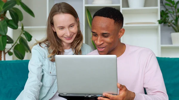 Fröhliches gemischtrassiges Paar surft gemeinsam auf Laptop, sitzt zu Hause auf Sofa — Stockfoto