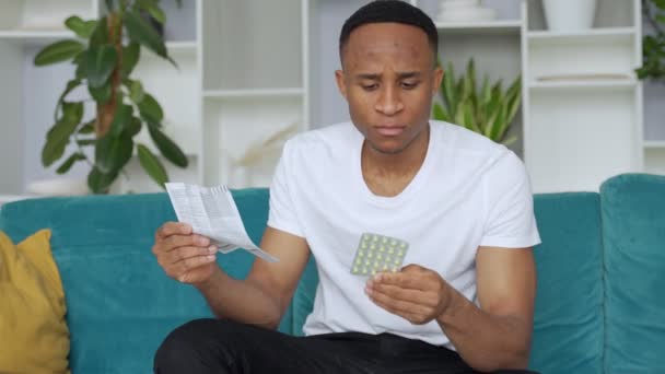 Uomo nero solo seduto sul divano malato istruzioni di lettura come prendere le pillole concentrate — Video Stock