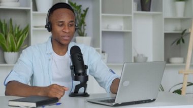 Podcast konsepti - kulaklıkla kulaklık takan mutlu genç siyahi adam ses blogcusu ve merkez ofisteki mikrofon yayını