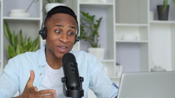 Podcast konsepti - kulaklıkla kulaklık takan mutlu genç siyahi adam ses blogcusu ve merkez ofisteki mikrofon yayını — Stok video