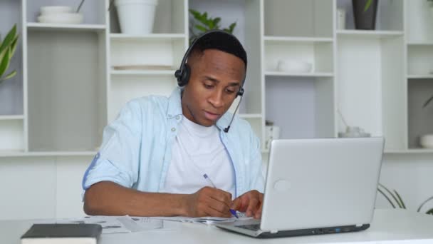 Konzentrierter schwarzer Berater mit Headset blickt auf einen Laptop — Stockvideo