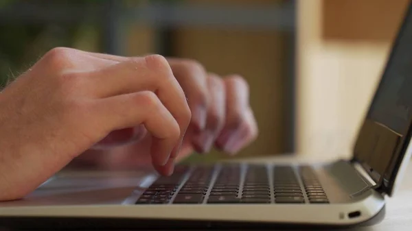 Primer plano plano de manos masculinas escribiendo en el ordenador portátil mientras está sentado en el escritorio de la oficina en el interior. Hombre dedos tocando y mensajes de texto en el teclado de la computadora mientras trabaja en el gabinete. — Foto de Stock