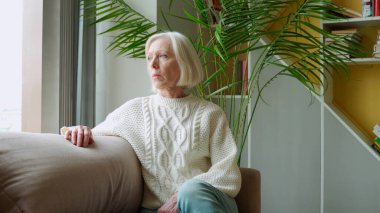 Yaşlı kadın sandalyede oturuyor ve pencereden bakıyor..
