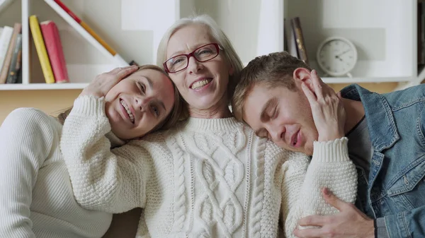 笑着年长的妈妈抱着她的女儿和儿子，坐在沙发上 — 图库照片