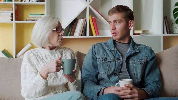 Hijo adulto visita a la madre mayor, disfrutar de agradable charla amistosa cálida en ambiente informal beber té sentado en el sofá —  Fotos de Stock