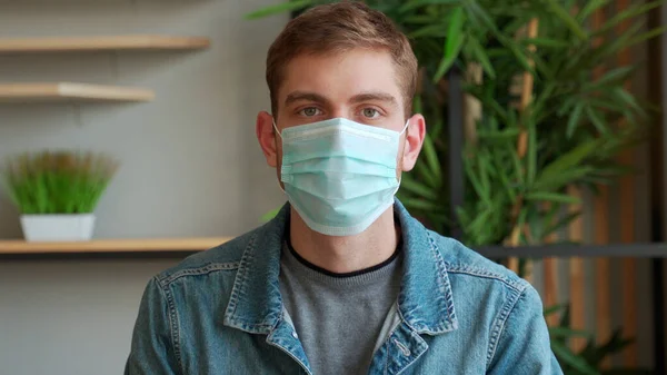 Homem retrato em máscara médica olhando para a câmera em casa. Pandemia. — Fotografia de Stock