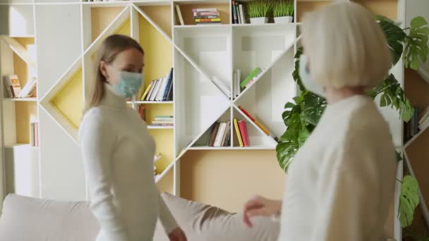 Äldre kvinna och ung kvinna med ansiktsmasker hälsar varandra genom att röra vid armbågarna på kontoret — Stockvideo