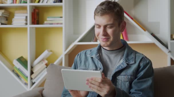 Uomo sorridente utilizzando tablet relax sul divano in ufficio moderno.Concetto di giovani uomini d'affari che lavorano a casa — Video Stock