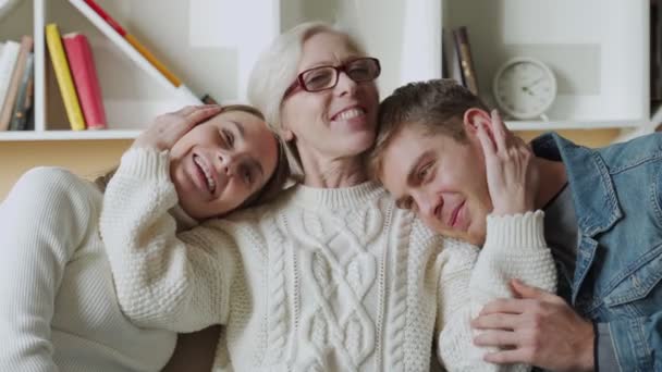 Tersenyum ibu tua memeluk putri dan anaknya sambil duduk di rumah di sofa — Stok Video