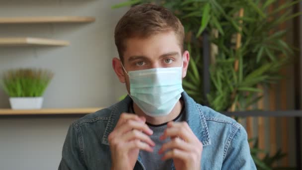 의료용 마스크를 쓴 남자가 집에 서 있는 카메라를 보고 있습니다. 세계적 유행병. — 비디오