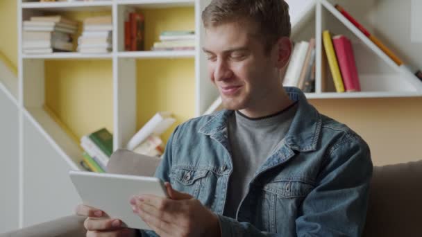 Uomo sorridente utilizzando tablet relax sul divano in ufficio moderno.Concetto di giovani uomini d'affari che lavorano a casa — Video Stock