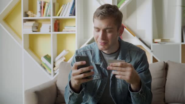 Online betalen. Man met debetkaart en smartphone om thuis te winkelen — Stockvideo