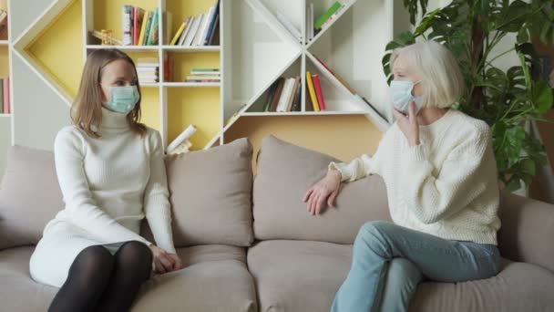 Putri dan ibu senior mengenakan masker medis yang bersenang-senang berbicara di rumah, wanita lanjut usia berusia dari dua generasi menikmati percakapan — Stok Video