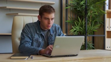 Ofiste otururken dizüstü bilgisayarda çalışan gülümseyen adam.