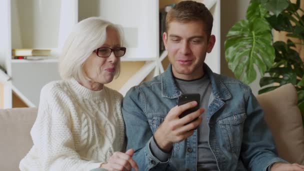 Smiling middle-aged mother rest with grown-up son using smartphone together, family weekend with senior mom browsing wireless Internet on cellphone — Stok Video