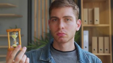 Ofiste kum saatine bakan bir adam bir şey düşünüyor.