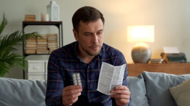 Genç adam evdeki kanepede oturan haplardan talimatları okuyor.