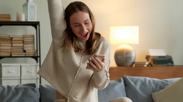 Mujer recibiendo buenas noticias de notificación a través del teléfono móvil. Chica celebrando la victoria en línea usando el teléfono celular — Foto de Stock