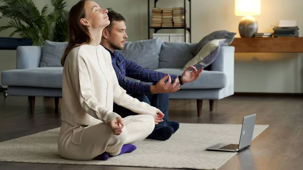 Práctica de yoga en línea. Pareja meditando en casa cerca del portátil — Foto de Stock