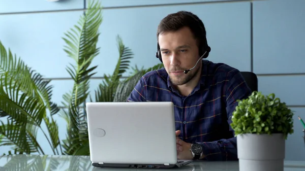 Empleado sonriente en auriculares usando laptop, mirando la pantalla, haciendo videollamadas o viendo webinar — Foto de Stock