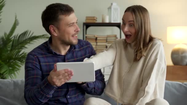 Opgewonden gelukkig familie paar op zoek naar digitale tablet voelen winnaars dolblij met de loterij winnende inzet bod, vieren goed internet nieuws. — Stockvideo
