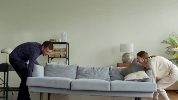 Szczęśliwa młoda para przenosi nową kanapę do salonu, upada na nią, aby odpocząć. — Wideo stockowe