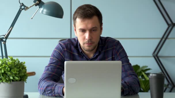 Портрет бизнесмен сидит за ноутбуком в офисе, работает, а затем смотрит в камеру — стоковое видео
