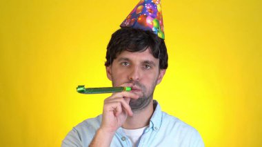 Üzücü üzgün, doğum günü şapkalı sıradan bir adam sarı arka plan stüdyosunda izole edilmiş bir parti gününü kutluyor. İnsanların yaşam tarzı yeni yıl tatili konsepti