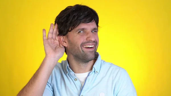 Fun Mann 30 Jahre alt isoliert auf gelbem Wandhintergrund Studio. Menschen aufrichtige Emotionen Lifestyle-Konzept. Versuchen Sie beiseite zu sehen, wie Sie mit der Hand am Ohr Geheimnisse belauschen — Stockfoto